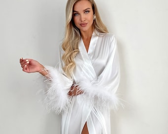 May include: A white satin robe with feather trim on the cuffs. The robe has a long, flowing silhouette and a deep V-neckline.