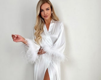 May include: A white satin robe with feather trim on the cuffs. The robe has a long, flowing silhouette and a deep V-neckline.