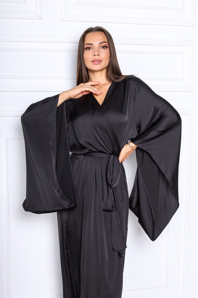 May include: A black satin robe with long, wide sleeves and a wrap closure. The robe has a V-neckline and a sash tie at the waist.
