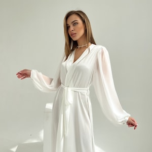 Puede incluir: Una bata de sat&eacute;n blanco con mangas transparentes y cintur&oacute;n a juego. La bata presenta un escote en V con detalles de perlas y pu&ntilde;os abotonados. El dise&ntilde;o largo y fluido es ideal.