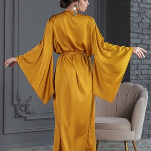 May include: A long, mustard yellow satin robe with wide, flowing sleeves and a sash tie at the waist.