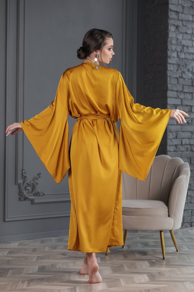May include: A long, mustard yellow satin robe with wide, flowing sleeves and a sash tie at the waist.