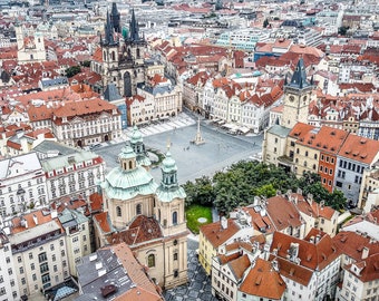 Könnte beinhalten: Eine Luftaufnahme eines großen, gepflasterten Platzes in einer europäischen Stadt. Der Platz ist umgeben von Gebäuden mit roten Ziegeldächern. Auf den Gebäuden befinden sich mehrere hohe, spitze Türme. Der Platz ist leer, bis auf ein paar Leute, die herumlaufen.
