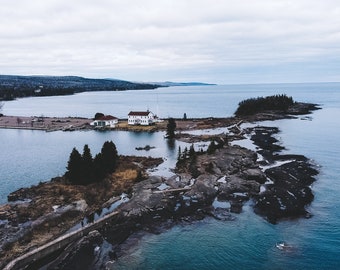 Könnte beinhalten: Luftaufnahme eines weißen Hauses mit rotem Dach auf einer kleinen Insel mit felsigen Ufern. Die Insel ist von blauem Wasser umgeben und im Hintergrund befindet sich eine größere Landmasse.