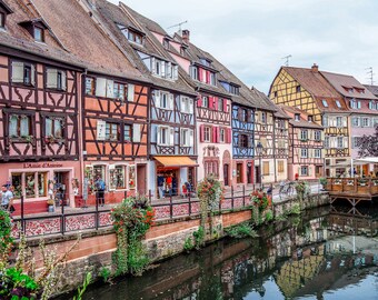 Könnte beinhalten: Eine Reihe von bunten Fachwerkhäusern säumen einen Kanal in einer europäischen Stadt. Die Gebäude haben eine Vielzahl von Farben, darunter rosa, gelb, blau und grün. Der Kanal spiegelt die Gebäude und den Himmel wider. Das Schild am Gebäude lautet "L'Amie d'Antoine".