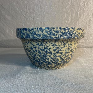 May include: A small, round ceramic bowl with a speckled blue and cream pattern. The bowl has a slightly flared rim and a rounded base. The speckled design covers the entire exterior of the bowl, creating a rustic, vintage aesthetic.