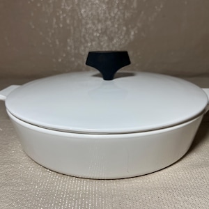 May include: White oval casserole dish with a matching lid and a black handle. The dish has two small handles on either side. A simple, elegant design for serving and cooking.