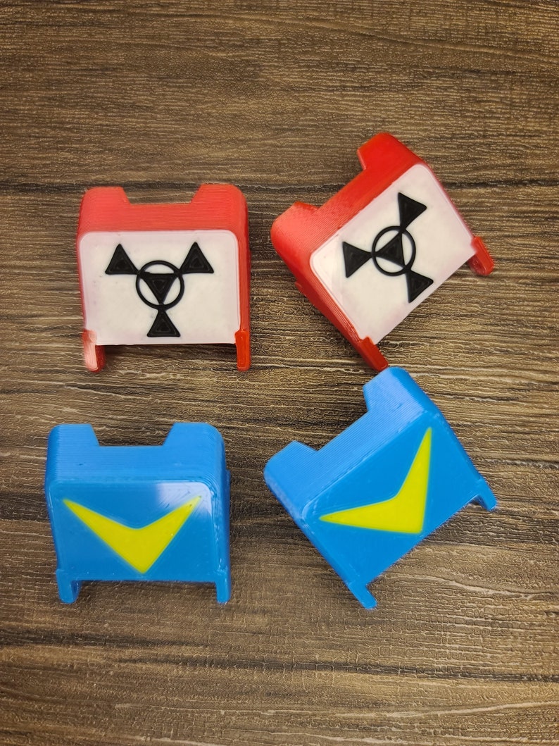 May include: Four plastic game pieces, two red and two blue. The red pieces have a white background with a black radiation symbol. The blue pieces have a yellow chevron shape on a blue background.