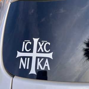 Könnte beinhalten: Ein weißer Vinyl-Aufkleber mit einem Kreuz und dem Text "IC XC NI KA" auf einem schwarzen Autofenster.