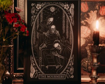 May include: A black framed print with a white illustration of three skeletons in a mourning scene. The print is titled "THE MOURNERS".