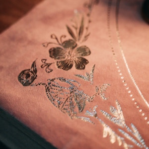 May include: A pink velvet fabric with a silver floral design. The design features a large flower and smaller leaves.