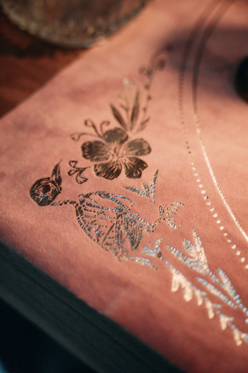 May include: A pink velvet fabric with a silver floral design. The design features a large flower and smaller leaves.