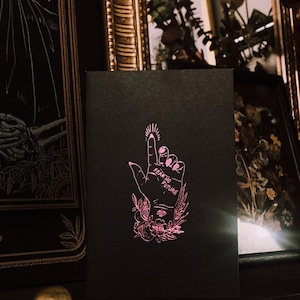 May include: A black card with a pink illustration of a hand with the words "Fear No Future" written on the palm. The hand is surrounded by flowers and leaves.