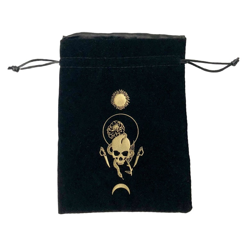 May include: Black velvet pouch with a gold drawstring closure. The pouch features a gold design of a skull with a snake wrapped around it, surrounded by a flower and a sun and moon symbol.