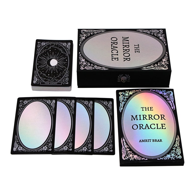 Peut inclure: Une bo&icirc;te noire avec un design holographique iridescent et le texte "The Mirror Oracle" sur le devant. La bo&icirc;te contient un jeu de cartes avec un design holographique similaire et le texte "The Mirror Oracle Amrit Brar" sur le devant.