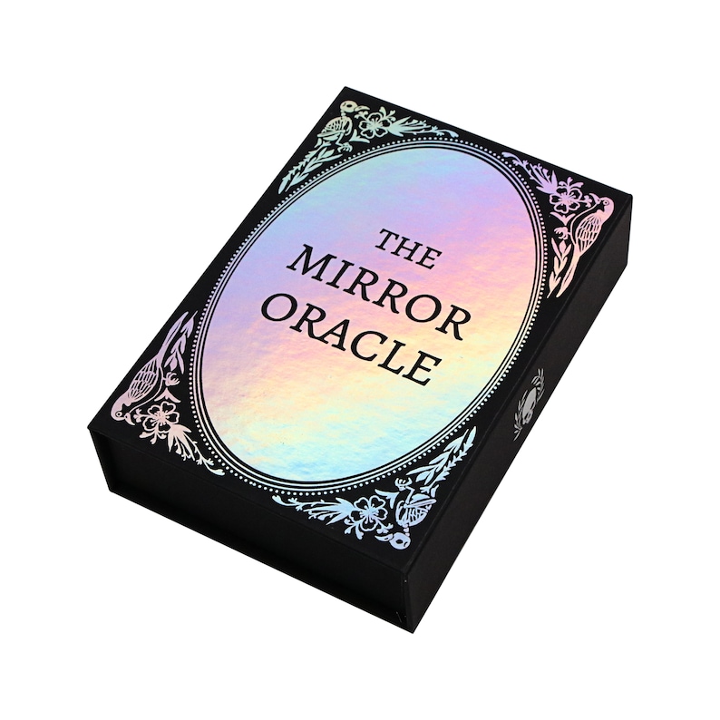 Peut inclure: Une bo&icirc;te noire avec un ovale holographique iridescent sur le devant. L'ovale a une bordure noire et des motifs floraux orn&eacute;s. Le texte "THE MIRROR ORACLE" est imprim&eacute; en noir &agrave; l'int&eacute;rieur de l'ovale.