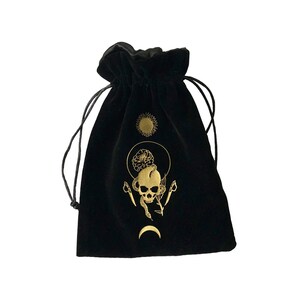 May include: Black velvet pouch with a gold skull and snake design. The pouch features a sun, moon, and floral accents.