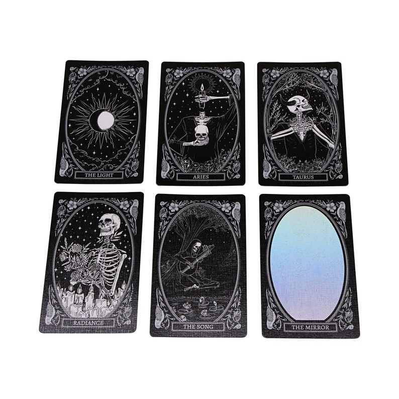 Peut inclure: Six cartes de tarot noires avec des illustrations blanches. Les cartes sont intitul&eacute;es "The Light", "Aries", "Taurus", "Radiance", "The Song", et "The Mirror".