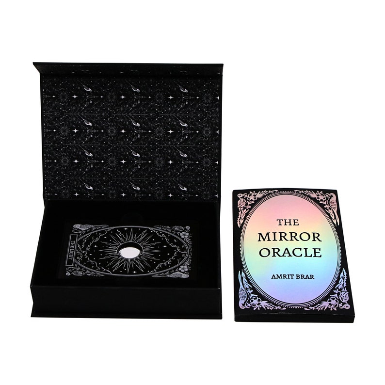 Peut inclure: Une bo&icirc;te noire contenant un jeu de cartes holographique. Le jeu de cartes pr&eacute;sente un motif blanc avec un soleil et une lune. La bo&icirc;te est orn&eacute;e d'un motif noir et blanc &agrave; l'int&eacute;rieur. La bo&icirc;te du jeu de cartes porte l'inscription "The Mirror Oracle" et "Amrit Brar" sur le devant.