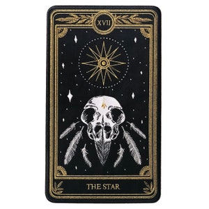 May include: Black and gold tarot card with the number XVII and the words "THE STAR" on it. The card features a white embroidered skull with feathers and a star with a circle in the center.