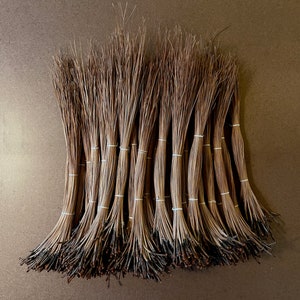 May include: A bundle of 25 natural brown pine needles tied together with white string. The needles are arranged in a fan shape and are ready for use in crafts or floral arrangements.
