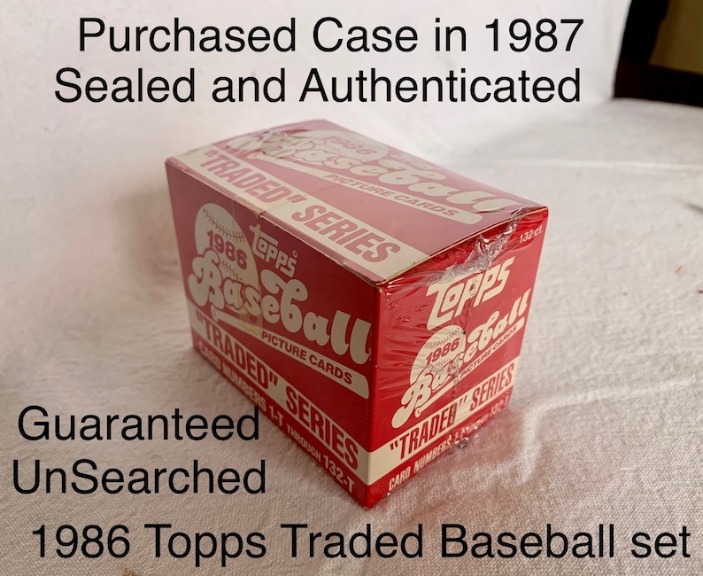 May include: A sealed box of 1986 Topps Traded Baseball cards. The box is red and white with the Topps logo and the words "1986 Topps Traded Baseball" printed on it. The box is sealed with plastic wrap.