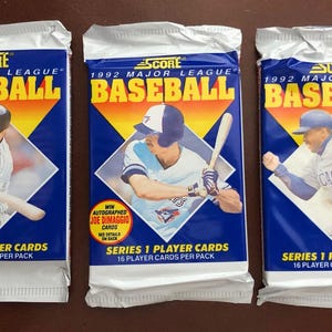 May include: Three unopened packs of 1992 Score Major League Baseball cards. Each pack features a baseball player image in a diamond shape against a blue background with yellow and orange accents. The packs are sealed in white foil.