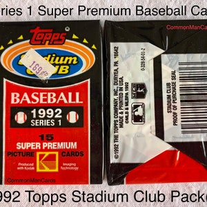 May include: Two unopened packs of 1992 Topps Stadium Club Series 1 baseball cards. The packs are black with red and white accents. The front of the pack features the Topps logo, the words "BASEBALL" and "1992 SERIES 1". The back has a barcode.