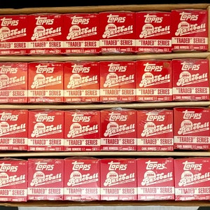 May include: A box of 24 unopened 1986 Topps Baseball "Traded" Series packs. The packs are red, white, and blue with the Topps logo and the words "1986 Baseball" and "Traded" Series printed on them.