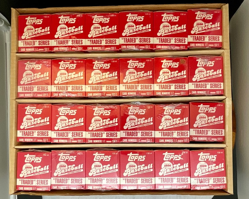 May include: A box of 24 unopened 1986 Topps Baseball "Traded" Series packs. The packs are red, white, and blue with the Topps logo and the words "1986 Baseball" and "Traded" Series printed on them.