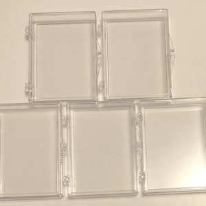 May include: Five clear plastic display boxes with hinged lids. The boxes are rectangular and have a smooth, glossy finish.