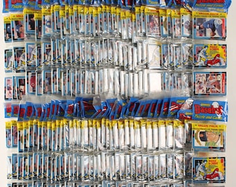 Può includere: Una collezione di pacchetti sigillati di figurine di baseball, disposti in file e colonne. I pacchetti sono principalmente blu e gialli, con il testo "Donruss Baseball Puzzle and Cards" visibile. Ogni pacchetto contiene diverse figurine.