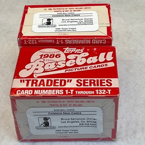 May include: Two red and white cardboard boxes of 1986 Topps Traded Baseball cards. The boxes are sealed and feature the Topps logo, the year 1986, and the text "Traded" series. The boxes also include the card numbers 1-T through 132-T.