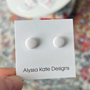 May include: A pair of white round stud earrings on a white card with the text "Alyssa Kate Designs".