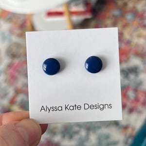 May include: A pair of blue stud earrings on a white card with the text "Alyssa Kate Designs".