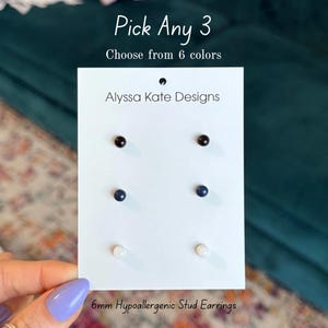 May include: A white card displays six 6mm hypoallergenic stud earrings in black, navy blue, and white. The card reads "Pick Any 3, Choose from 6 colors" and "Alyssa Kate Designs."