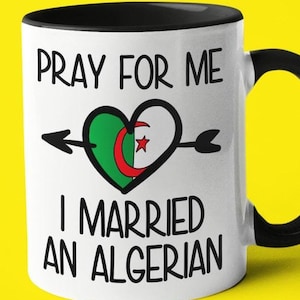 Peut inclure: Une tasse en céramique blanche avec un bord et une poignée noirs. La tasse présente un cœur noir et vert avec une flèche qui le traverse et le texte "Priez pour moi, j'ai épousé un Algérien".