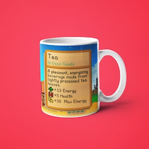 Op de afbeelding: Een witte keramische mok met een kleurrijk beeld van een videogame-item genaamd "Thee" uit het spel Stardew Valley. De afbeelding toont een beschrijving van het item, dat een drankje is dat de speler 13 energie, 5 gezondheid en 30 maximale energie geeft.