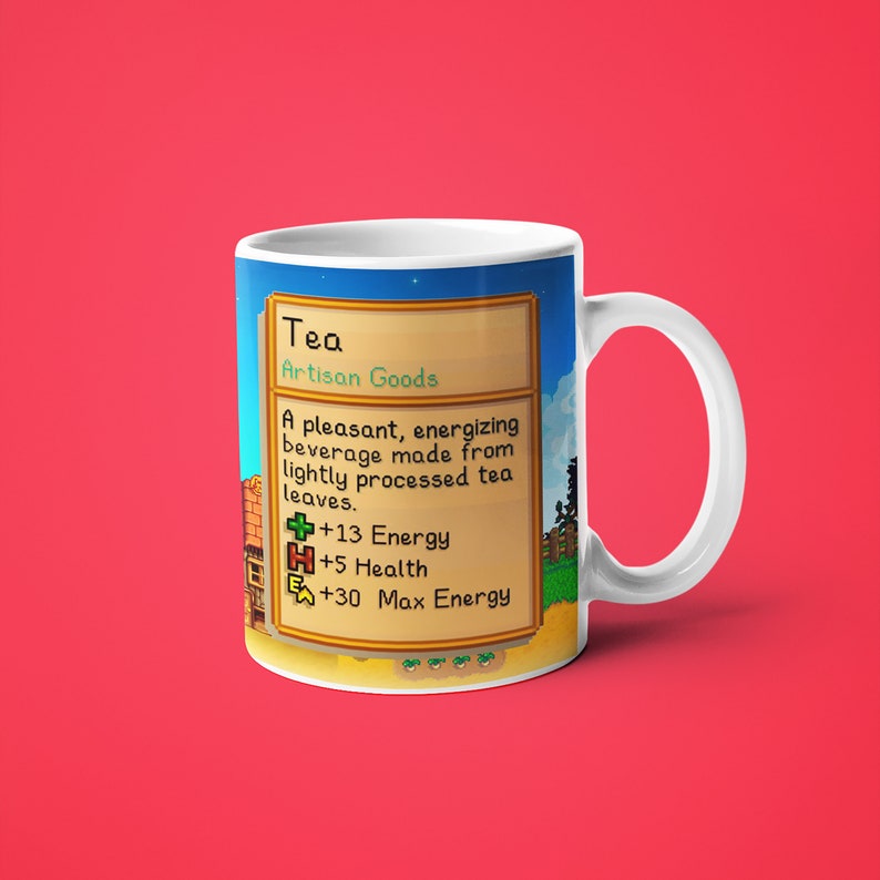 Op de afbeelding: Een witte keramische mok met een kleurrijk beeld van een videogame-item genaamd "Thee" uit het spel Stardew Valley. De afbeelding toont een beschrijving van het item, dat een drankje is dat de speler 13 energie, 5 gezondheid en 30 maximale energie geeft.