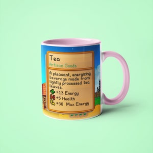 Op de afbeelding: Een roze en witte mok met een gepixelde afbeelding van een videogame-item genaamd "Thee". De afbeelding toont de tekst "Thee, Ambachtelijke producten, Een aangenaam, energiek drankje gemaakt van licht verwerkte theebladeren. +13 Energie +5 Gezondheid +30 Maximale energie".