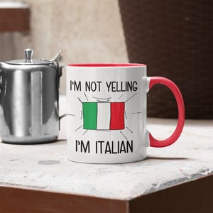 May include: White ceramic mug with a red rim and handle. The mug has a black graphic that says "I'm not yelling I'm Italian" with a cartoon drawing of the Italian flag.