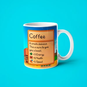 May include: White coffee mug with a pixelated design inspired by the video game Stardew Valley. The mug features a text box with the word "Coffee" and a description of the drink's effects: "It smells delicious. This is sure to give you a boost. +3 Energy +1 Health +1 Speed"