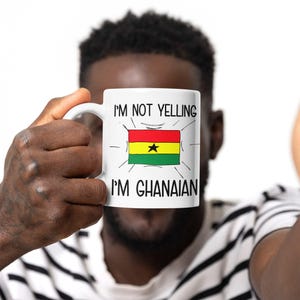 May include: White ceramic mug with a black and red design. The mug has the text "I'm not yelling I'm Ghanaian" and a cartoon image of the Ghanaian flag.