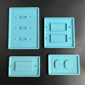 May include: Four light blue silicone molds for making different types of wall switches. The molds are rectangular and have raised edges. The first mold has three rectangular cutouts, the second mold has two rectangular cutouts, the third mold has one rectangular cutout, and the fourth mold has two round cutouts.