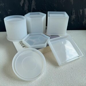 May include: Set of six white silicone moulds for crafting. The moulds are in various shapes, including a round cylinder, a square, a hexagon, and two different sized round coasters.