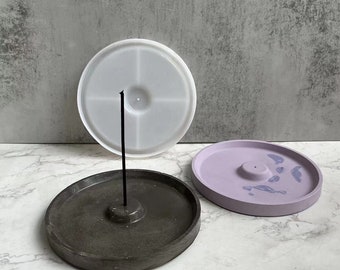 May include: Three round incense holders, one is white, one is light purple with blue swirls, and one is dark gray. The holders are made of concrete and have a small raised center for the incense stick.