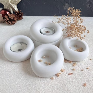 Puede incluir: Cuatro portavelas de cerámica blanca con un diseño de anillo. Cada portavelas tiene una pequeña hendidura en el centro para sostener una vela de té.
