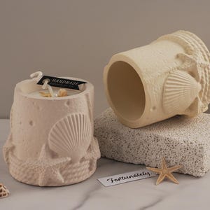 Puede incluir: Dos portavelas de cerámica blanca con un diseño de conchas marinas y estrellas de mar. Los portavelas son hechos a mano y tienen una etiqueta que dice "Handmade".