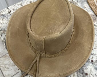 May include: A tan-colored cowboy hat with a wide brim and a braided band around the crown. The hat has a suede-like texture and a leather tie. The hat's brim measures approximately 14 inches in diameter.