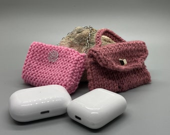 May include: Two pink knitted purses with a silver clasp and a white wireless charging case.
